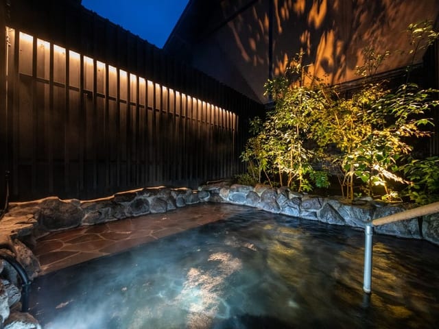 夜の露天風呂。ライトアップされた木立を背に湯気が立ちのぼる