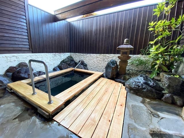 貸切露天風呂「愛の湯」。木のデッキに囲まれた石造りの湯船と石灯籠