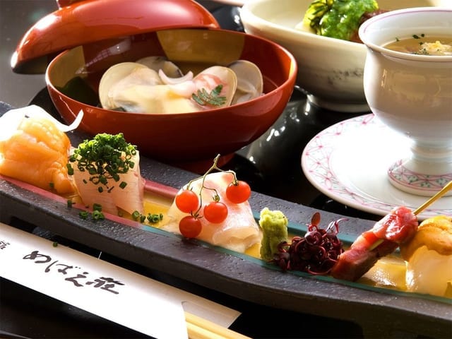 会席の一例。「めばえ荘」の箸袋を添えた前菜の細長い皿と、蛤の椀が並ぶ