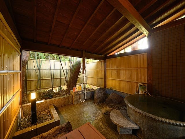信楽焼の陶器風呂が付いた離れの和洋室。木の庇の下に丸い湯船が据えられている