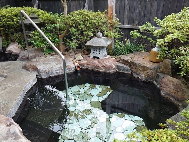 岩造りの専用露天風呂。石灯籠を配した庭に面し、竹の湯口から源泉が注ぐ