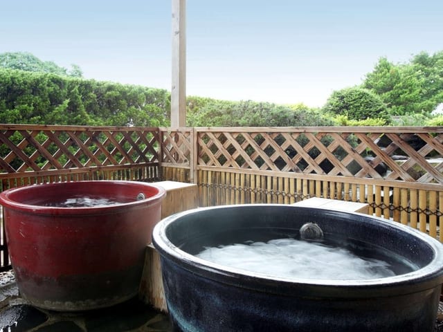 陶器の露天風呂。2つの大きな壺の湯船が竹垣と緑に囲まれている