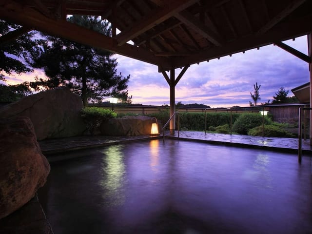夕暮れの露天風呂。東屋の下の湯面に紫の空が映っている