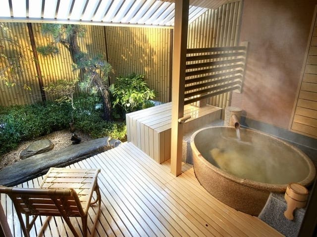 別邸「美悠」の客室露天風呂。ウッドデッキに据えた丸い石の湯船から湯気が立ち、松の植わる坪庭に面している