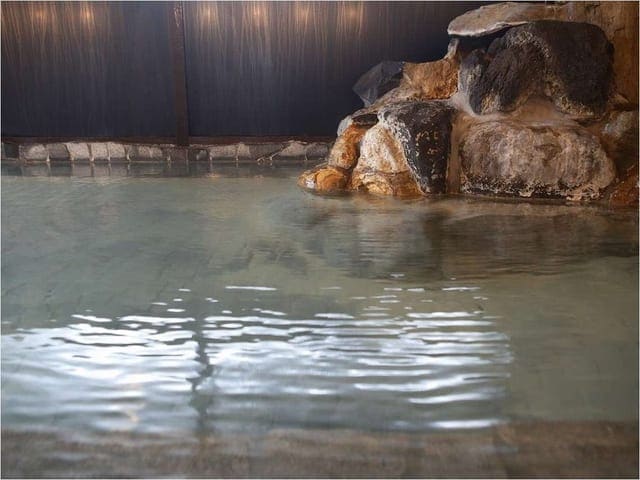 源泉かけ流しの湯船。岩を組んだ湯口から湯が注ぎ、湯気が立つ