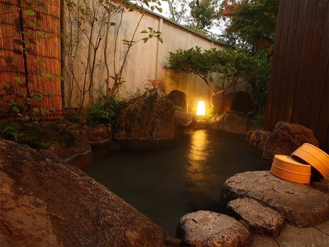 貸切露天風呂。夕闇のなか行灯の灯りが湯面に映り、湯桶が置かれている