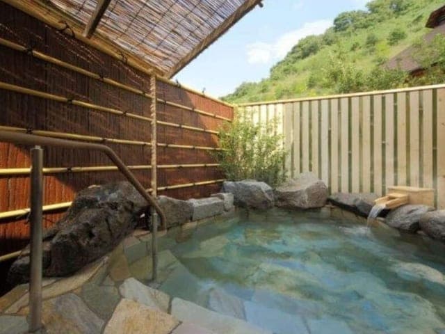 南部曲り家の湯の貸切風呂。木の湯船の向こうに竹垣と木々が見える
