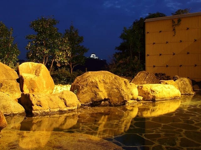 夜の露天風呂。ライトアップされた岩組みと琥珀色の湯面が広がる