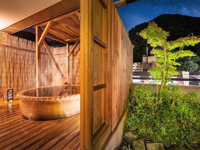 青森ヒバの丸い湯船を据えた露天。手すりの向こうに木々が茂る