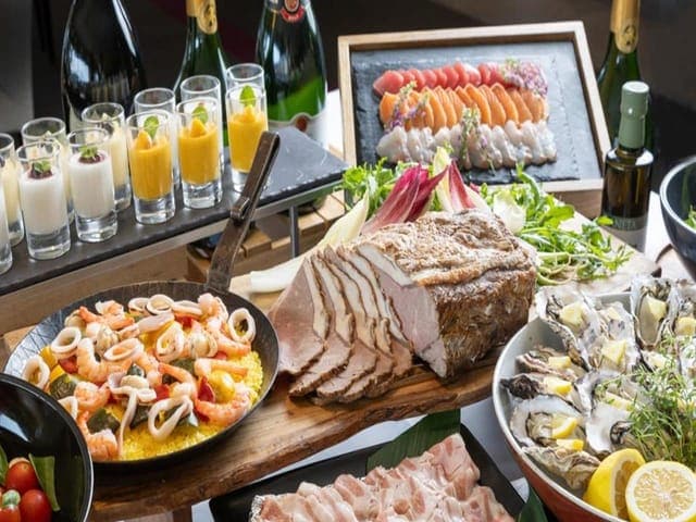ディナービュッフェの台。ローストした肉の塊、パエリア、牡蠣、小さなグラスのデザートが並ぶ
