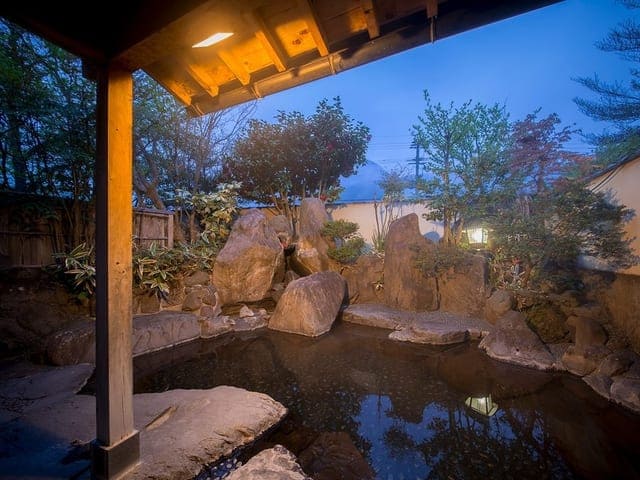 夜の露天風呂。庇の下の湯船に岩が組まれ、藍色の空が広がる