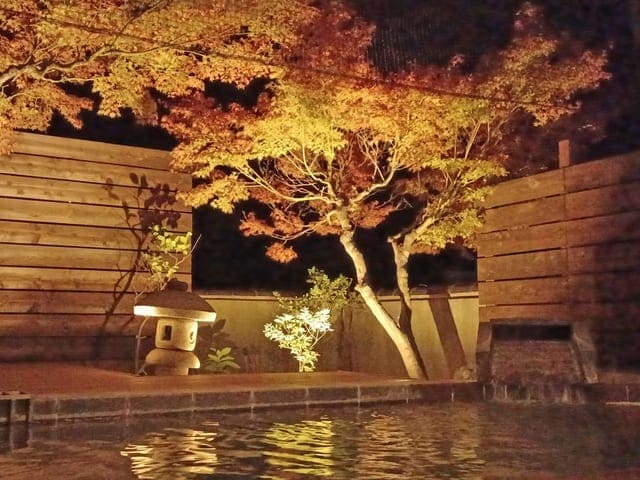 露天風呂。ライトアップされた紅葉と石灯籠が、湯面に映り込んでいる