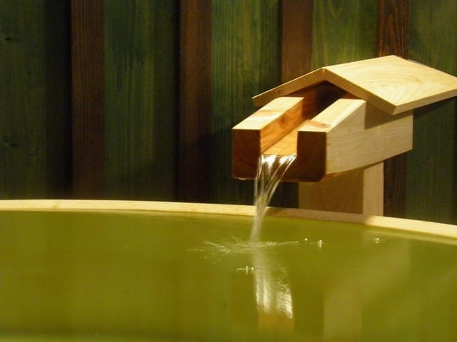 緑がかった湯の湯口。木の樋から湯が落ちる