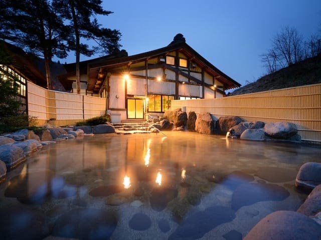 夕暮れの露天風呂「とよさわ乃湯」。湯気の向こうに宿の灯りがともる