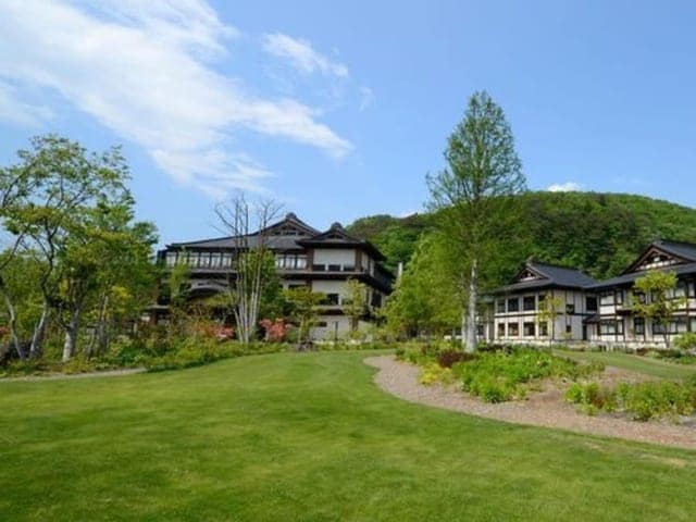 芝生の庭ごしに見る木造の本館。背後に山の緑が続く