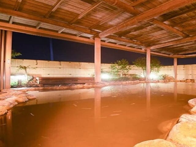夜の露天風呂。木の梁の下、茶褐色の湯が湯船を満たす