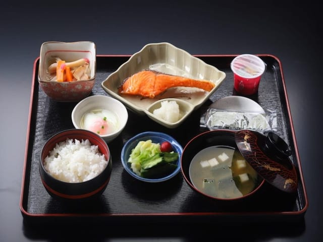 朝食の御膳。焼き鮭と小鉢、味噌汁が黒い盆に並ぶ