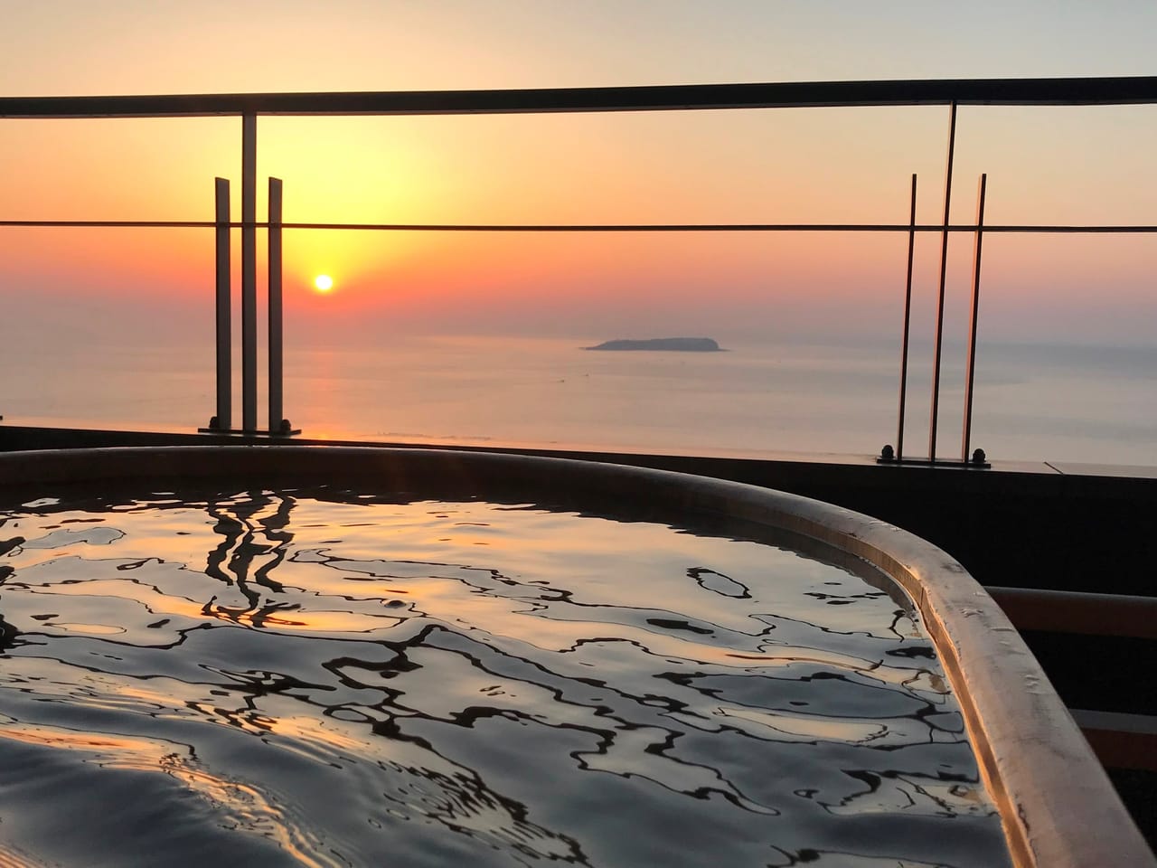 熱海さんがの客室露天風呂。湯船の先に相模湾が広がり、水平線の太陽が空をオレンジに染めている
